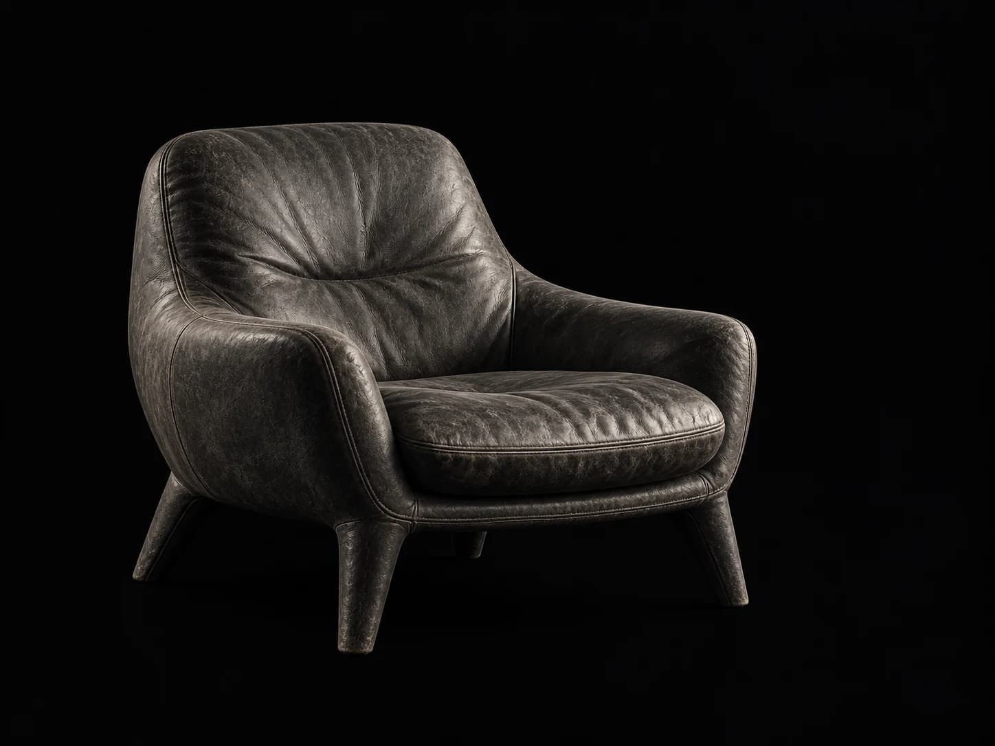 Understated worn charcoal leather lounge chair in a dark editorial studio.