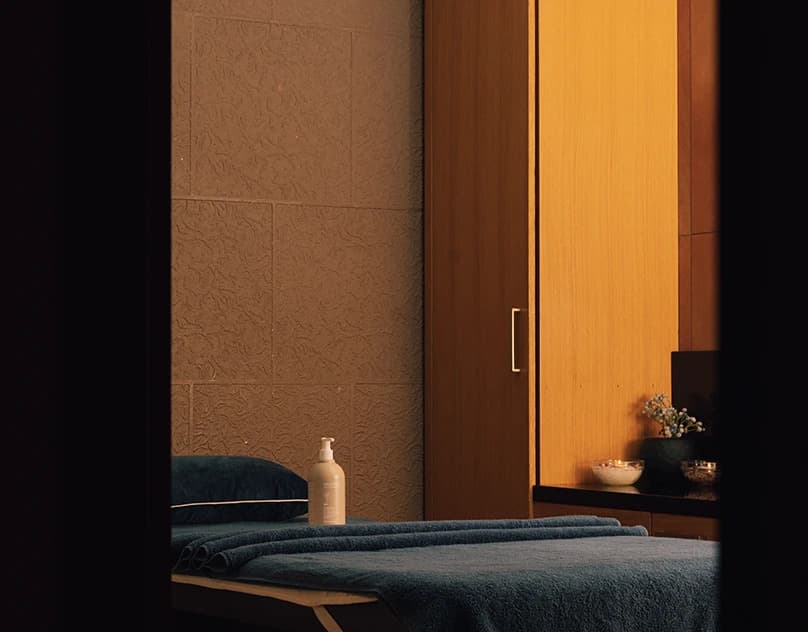 A Divan Erbil spa treatment room with a made-up massage bed, warm wood panelling and low even light.